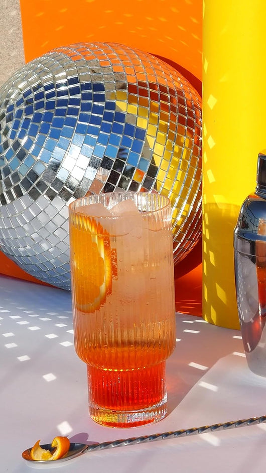 Cocktail in a textured glass with orange garnish, disco ball and bright background, ideal for vibrant party settings.
